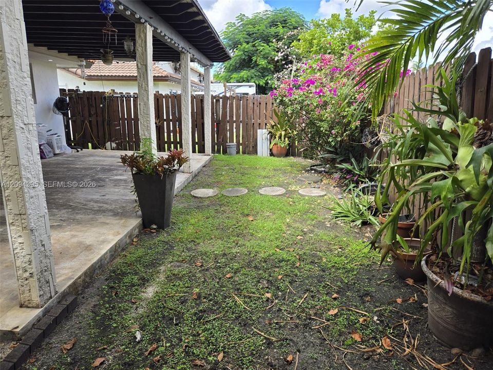 Covered patio featuring concrete flooring and textured support columns, complemented by a fenced backyard with concrete paver stepping stones and established landscaping