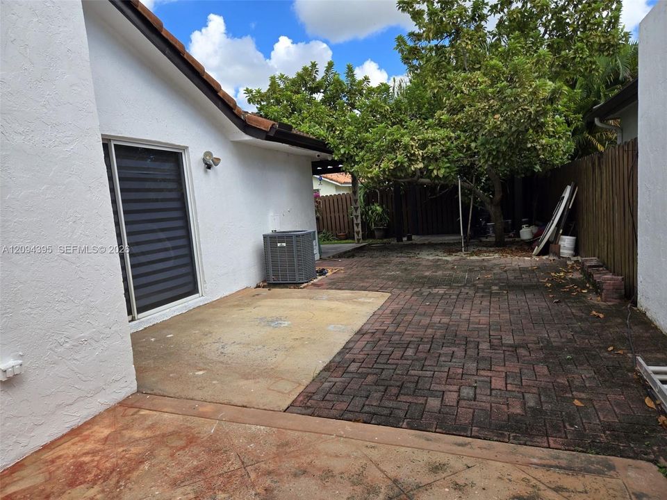 Rear exterior featuring a concrete patio, herringbone-pattern brick paver accents, and a wood privacy fence