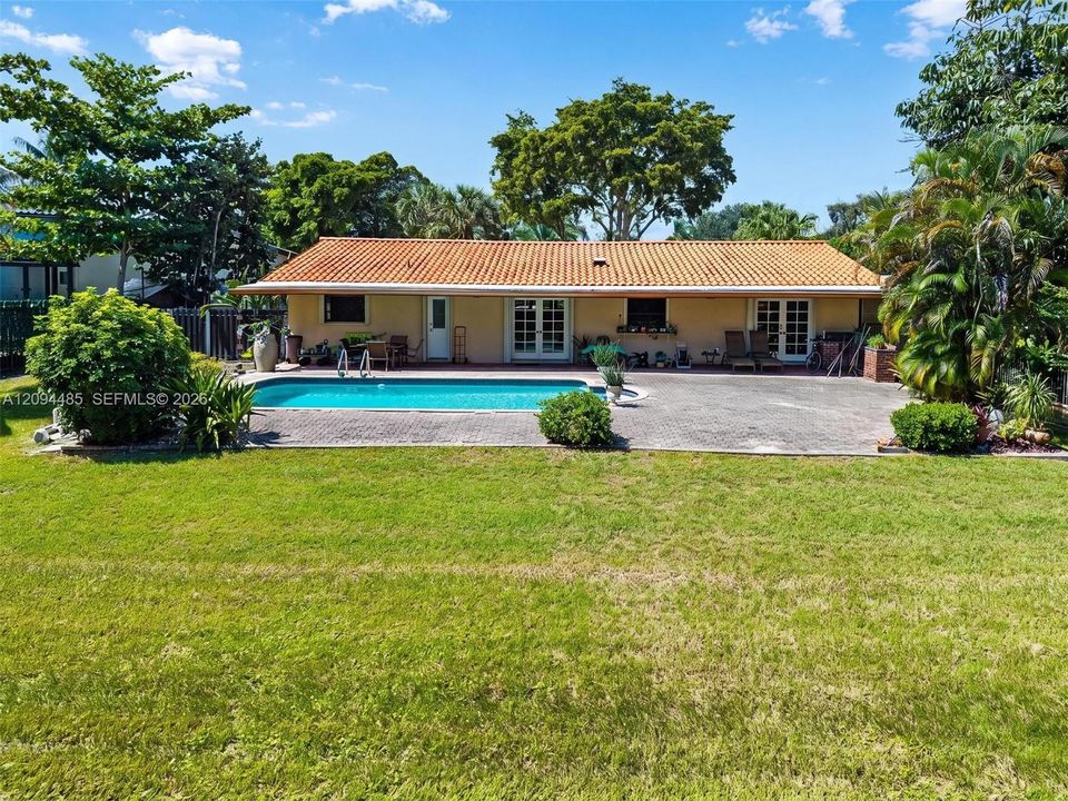 Exterior featuring a clay tile roof, rear swimming pool, paver patio, and lawn