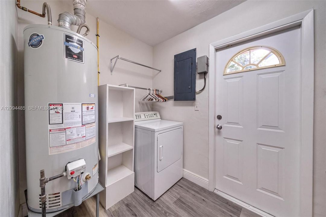 Utility area featuring wood-finish flooring, a white metal exterior door with a semi-circular transom window, and white built-in shelving