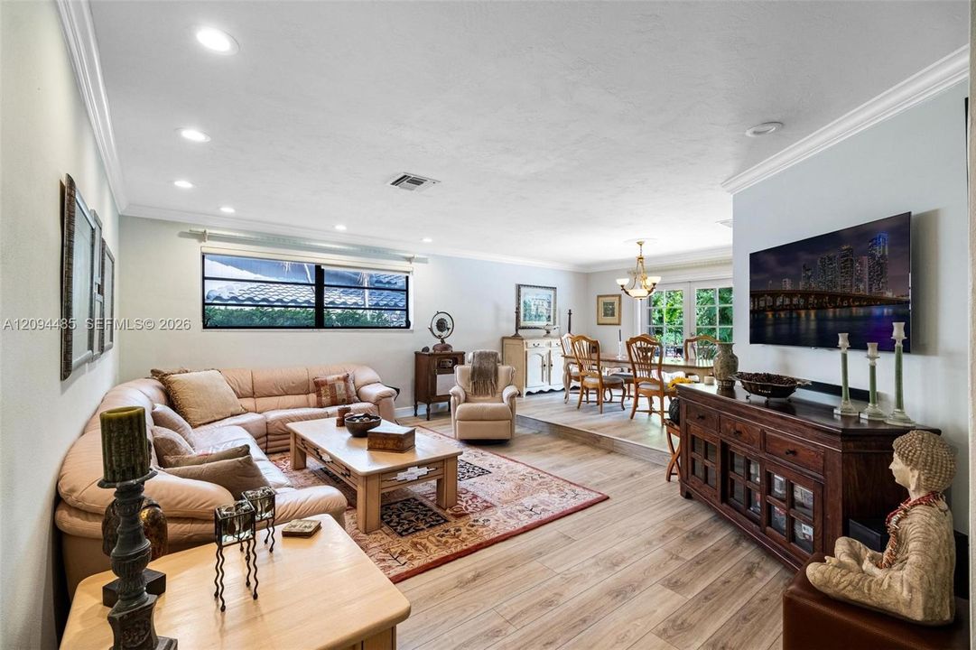 Open-concept interior featuring recessed lighting, crown molding, wood-finish flooring, and a raised platform area with glass-paned double doors