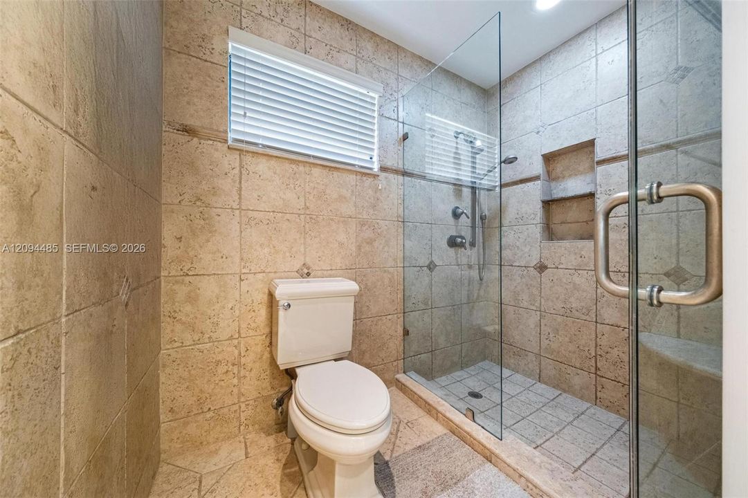 Walk-in shower featuring glass enclosure, built-in recessed shelving, wall-mounted shower head, and tile surround with integrated tile flooring