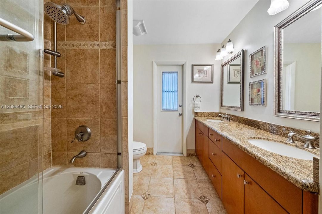 Bathroom featuring a dual-sink vanity with stone countertops, wood cabinetry, tile flooring with decorative inlay, and a glass-enclosed shower and tub combination with tile surround