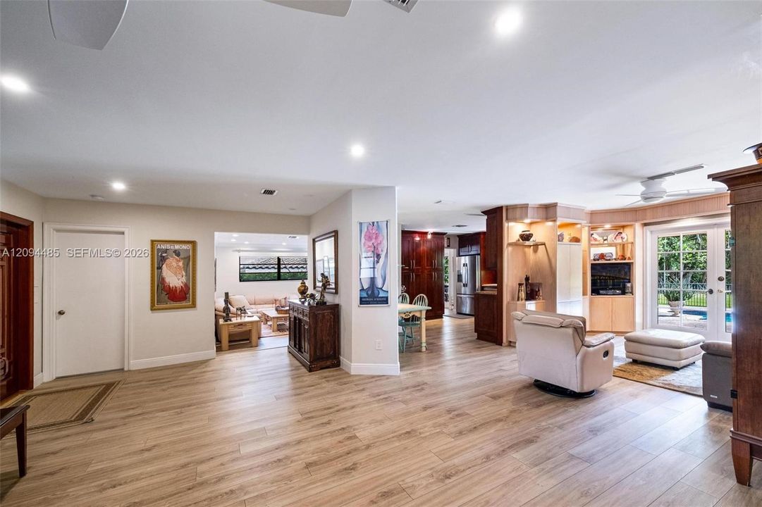 Open-concept interior featuring light wood-finish flooring, recessed lighting, built-in light wood cabinetry, and double glass doors providing exterior access
