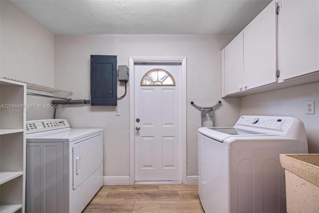Laundry area featuring wood-finish flooring, white upper wall-mounted cabinetry, integrated shelving, and a utility sink