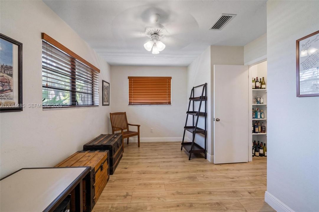 Room featuring wood-finish flooring, dual windows with horizontal blinds, a ceiling fan with integrated lighting, and a reach-in pantry