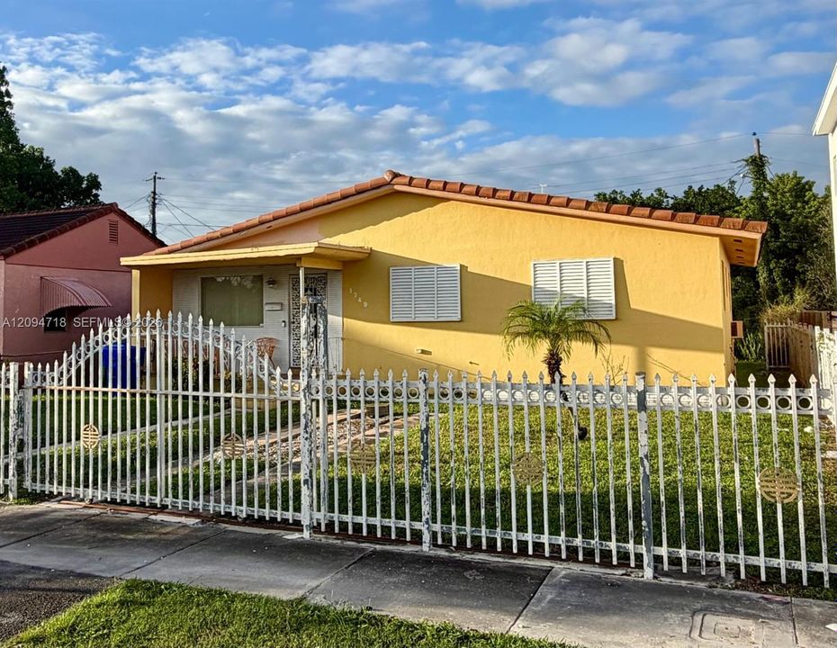 Stucco exterior featuring a low-slope clay tile roof, white louvered shutters, and a decorative metal perimeter fence