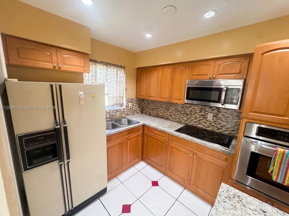 Kitchen featuring natural wood cabinetry, stone-finish countertops, mosaic tile backsplash, built-in stainless steel microwave and wall oven, and ceramic tile flooring