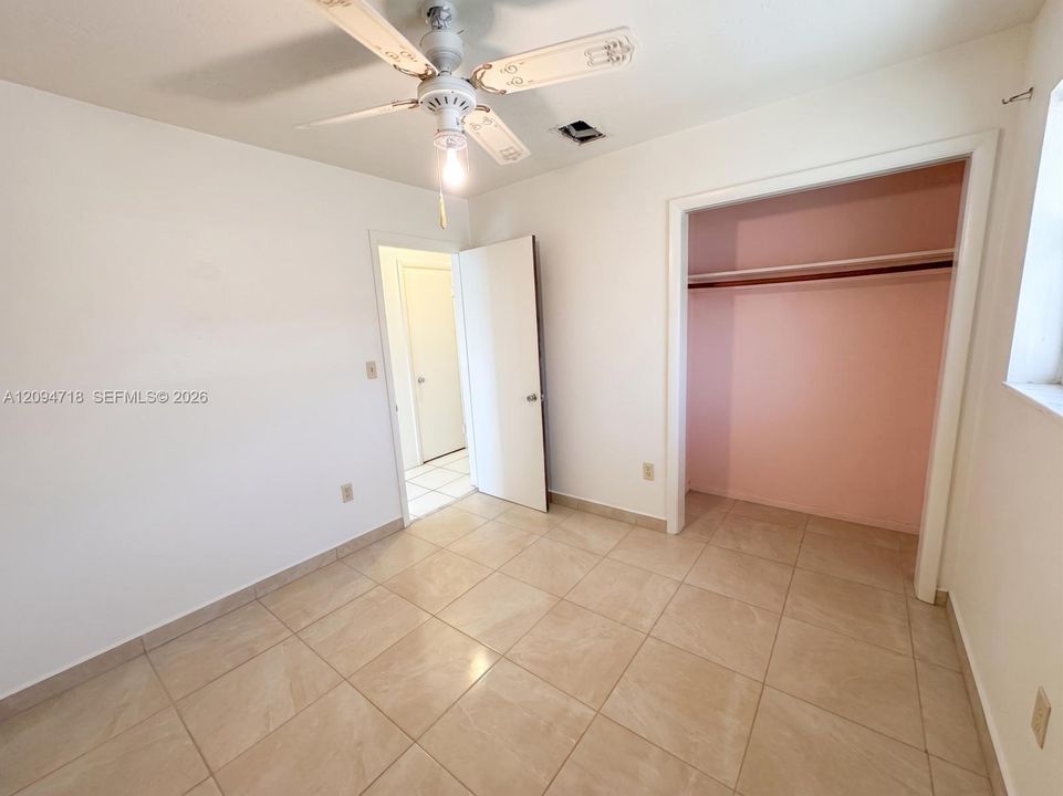 Neutral-toned floor tiles, white walls, built-in closet with shelving, and overhead ceiling fan with lighting