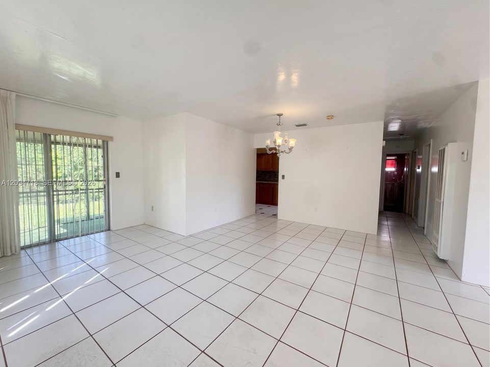 Open-concept interior featuring white ceramic tile flooring, sliding glass patio doors with security bars, and a multi-arm crystal-style chandelier