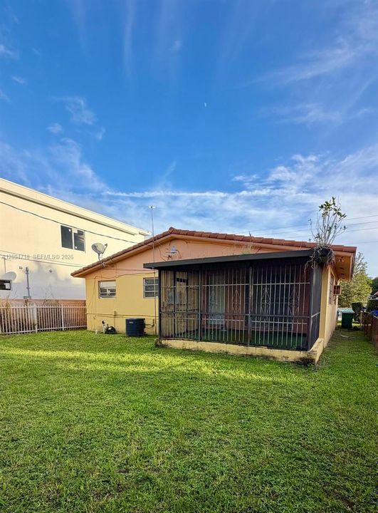 Exterior rear elevation featuring a covered screened-in porch, metal security bars, tile roofing, and a fenced yard