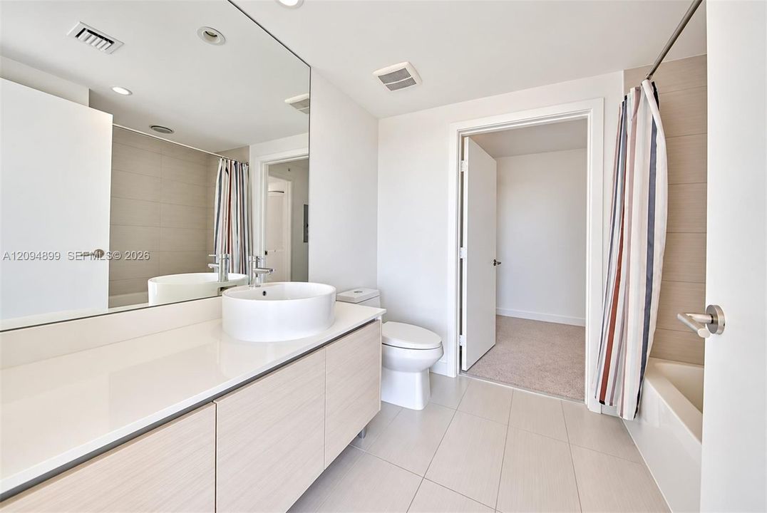 Bathroom featuring a light wood-finish vanity, white countertop, vessel sink, polished chrome faucet, and large wall-to-wall mirror