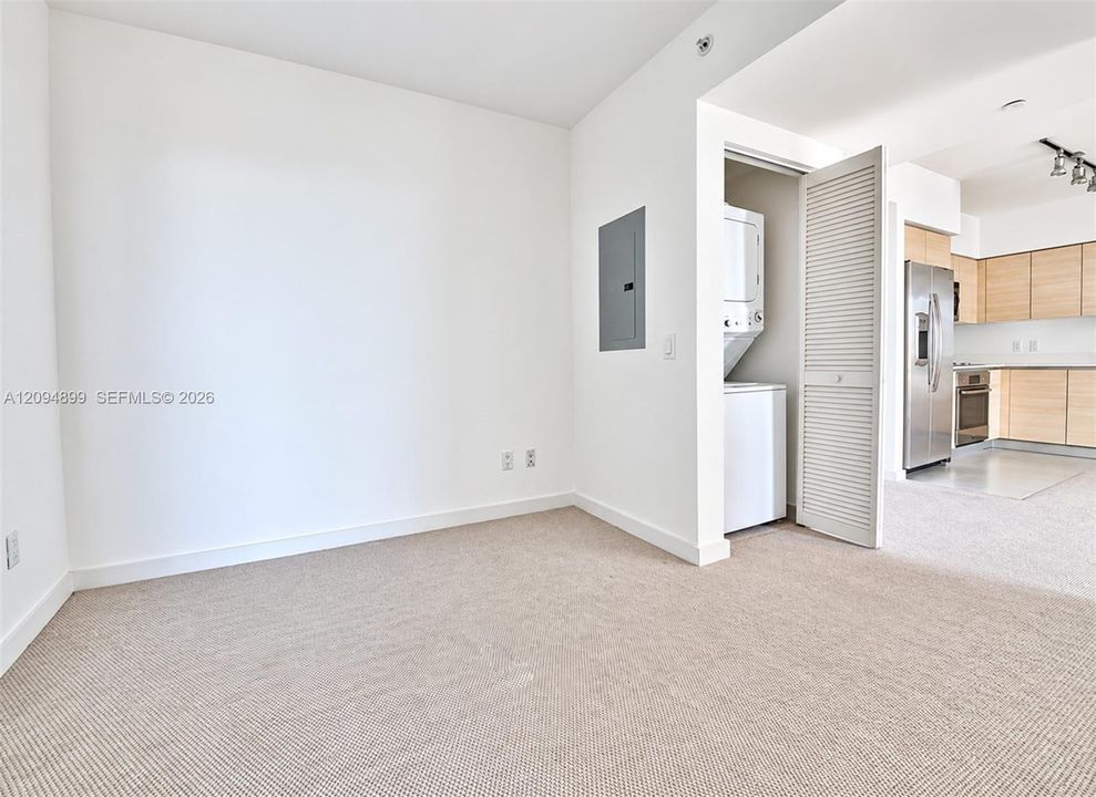 Neutral carpeted interior featuring a louvered-door laundry closet with a stackable washer and dryer, and flat-panel cabinetry in the kitchen