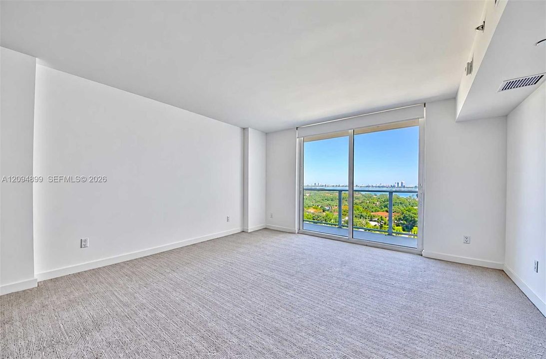 Floor-to-ceiling glass sliding door, neutral carpeting, and exterior metal railing featuring a horizon backdrop