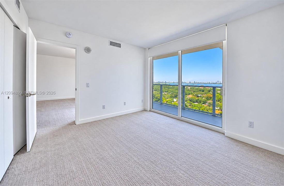 Floor-to-ceiling sliding glass door, private balcony with metal railing, carpeting, and natural light