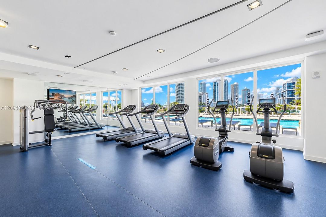 Fitness center featuring wall-to-wall mirrors, recessed lighting, and floor-to-ceiling windows with urban and swimming pool scenery