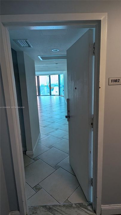 Entryway featuring large-format tile flooring with decorative stone inlays, recessed lighting, and expansive floor-to-ceiling windows