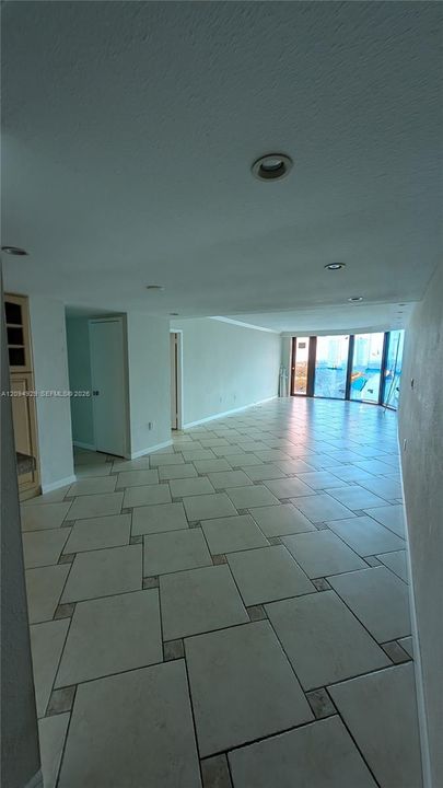 Open-concept floor plan featuring large-format tile flooring with decorative inlay accents, recessed ceiling lighting, floor-to-ceiling glass windows, and built-in cabinetry