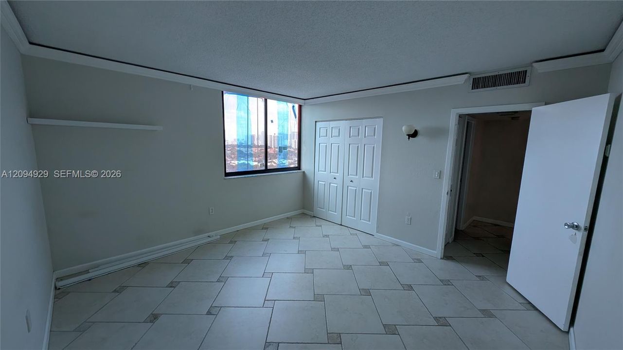 Room featuring large-format ceramic tile flooring with decorative inlay accents, a multi-pane window, dual-panel closet doors, and wall-mounted light fixtures