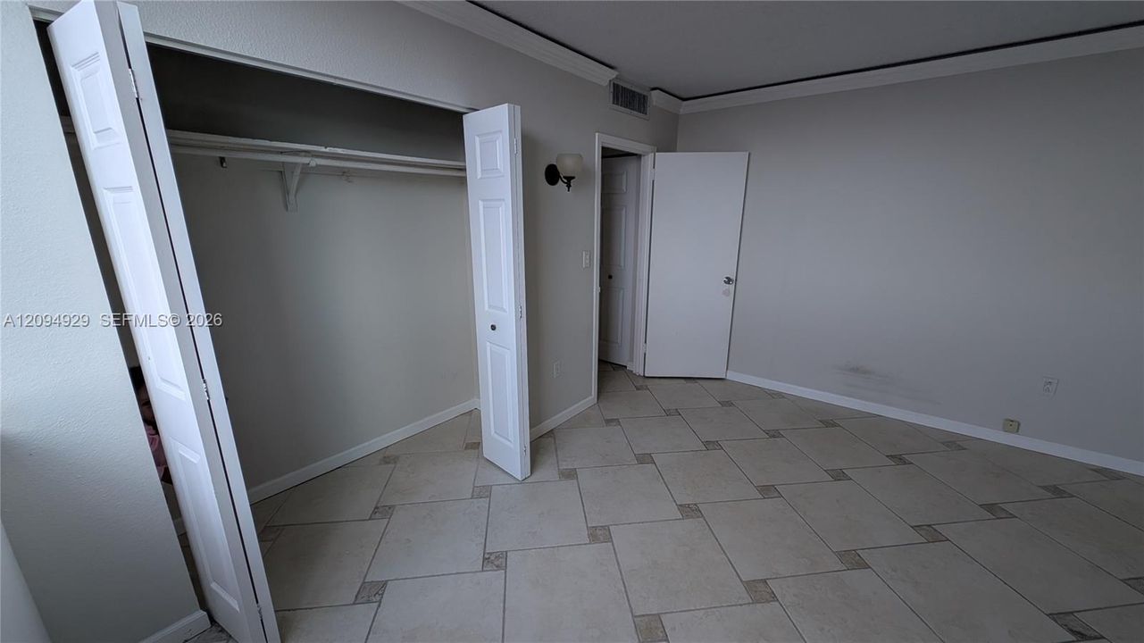 Neutral-toned room featuring large-format ceramic tile flooring with decorative stone inlays, crown molding, and a reach-in closet with double bifold doors