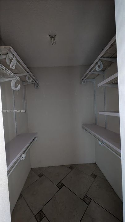 Walk-in closet featuring stone-finish floor tiles, multi-level wire shelving, and overhead lighting
