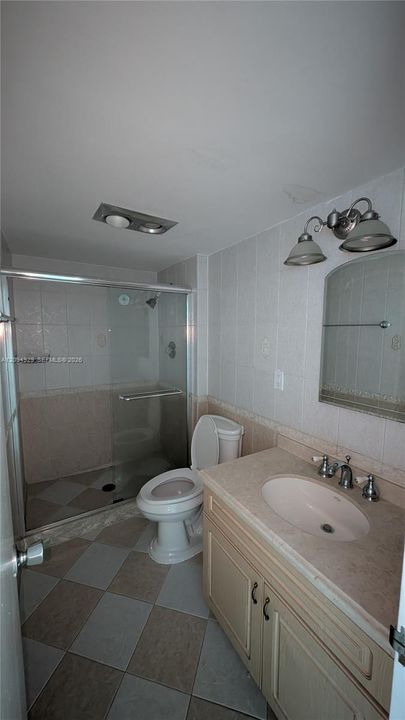 Bathroom featuring a walk-in shower with a glass enclosure, tile flooring in a checkerboard pattern, vanity with a solid-surface countertop and integrated sink, and an arched wall-mounted mirror
