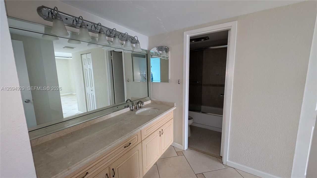 Bathroom vanity featuring a stone-surface countertop, integrated basin, multi-light fixture, full-width mirror, and tile flooring