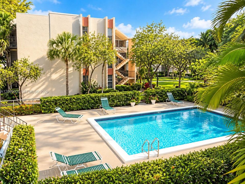 In-ground rectangular swimming pool with metal ladder, surrounded by a paved deck and manicured shrubbery