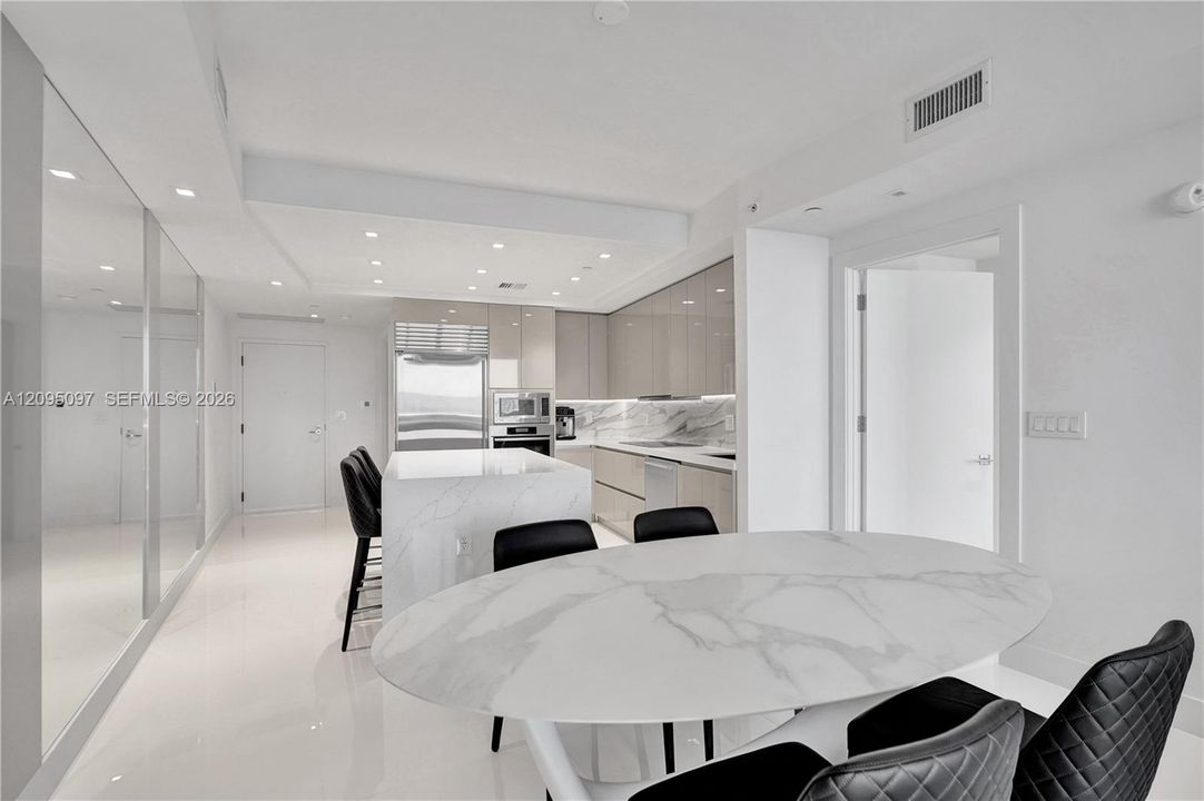 Contemporary kitchen featuring high-gloss cabinetry, stone-surface island, integrated stainless steel appliances, recessed lighting, and polished stone-finish flooring