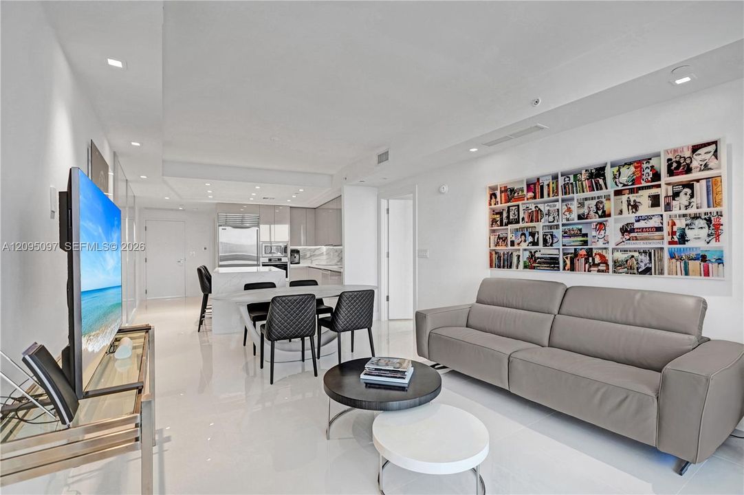 Open-concept interior featuring high-gloss flooring, recessed lighting, a built-in recessed shelving unit, and a kitchen equipped with stone-surfaced countertops and stainless steel appliances