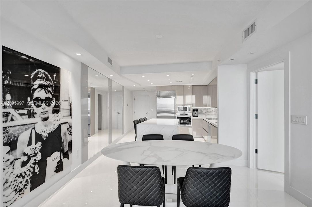 Open-concept kitchen featuring high-gloss cabinetry, a central island with stone-finish countertops, stainless steel appliances, recessed lighting, and polished stone flooring