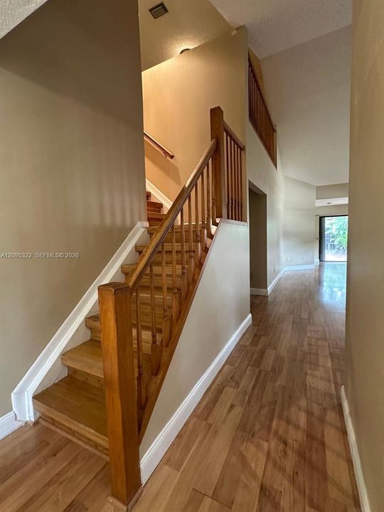 Staircase featuring wood treads and a stained wood railing, complemented by wood-finish flooring and a high-vaulted ceiling