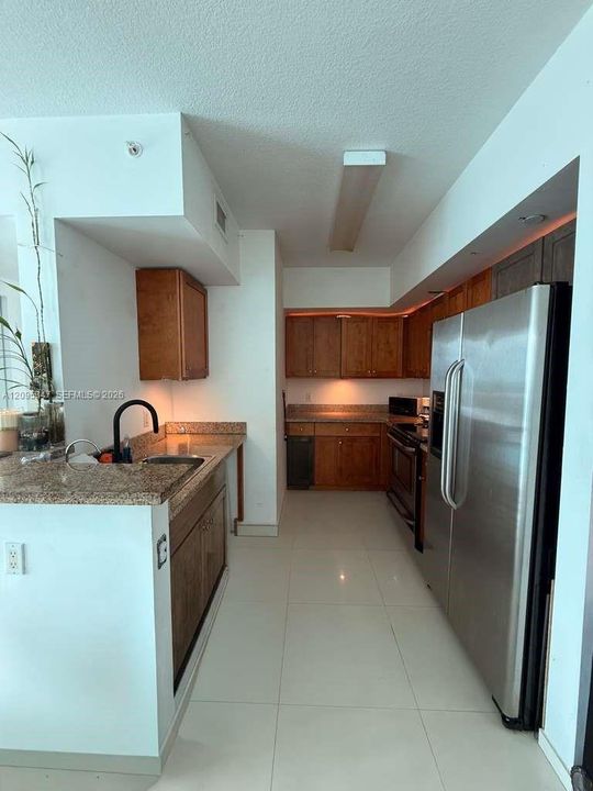 Kitchen featuring wood cabinetry, stone countertops, large-format tile flooring, stainless steel side-by-side refrigerator, and a matte black faucet