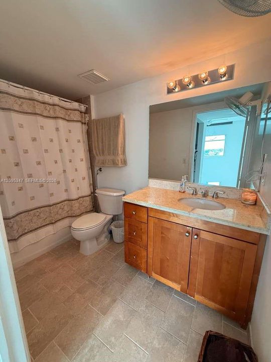 Bathroom featuring wood-finish cabinetry, stone-surface countertop with an integrated basin, large vanity mirror, and ceramic tile flooring