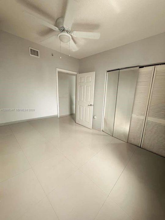Room featuring large-format tile flooring, a multi-panel door, sliding mirrored closet doors, and a ceiling-mounted fan with integrated lighting