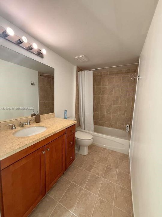 Bathroom featuring wood-finish cabinetry, stone-texture countertop, integrated porcelain sink, tiled tub surround, and ceramic tile flooring