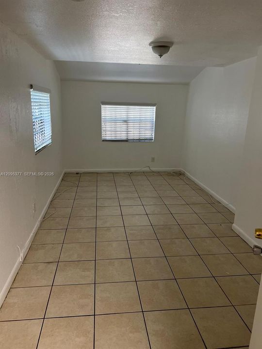 Interior room featuring large-format ceramic tile flooring, neutral wall finishes, and two windows equipped with horizontal blinds, illuminated by a flush-mount ceiling fixture