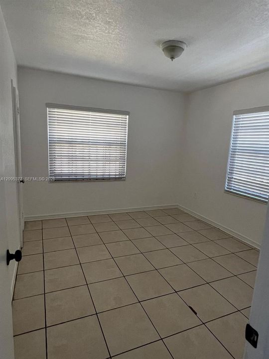 Neutral interior featuring light-toned ceramic tile flooring, two windows with horizontal blinds, and a flush-mount ceiling light fixture
