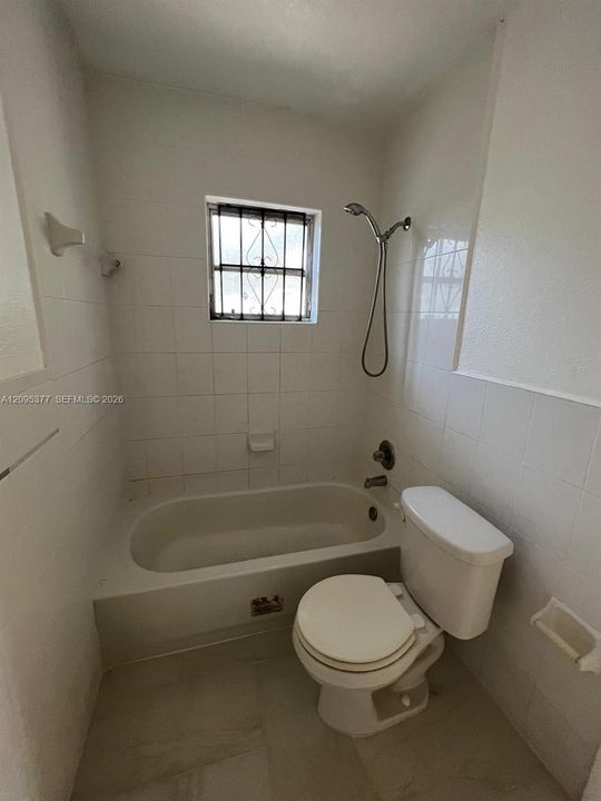 Full-height tiled walls, porcelain bathtub with a handheld shower fixture, and a window with security bars