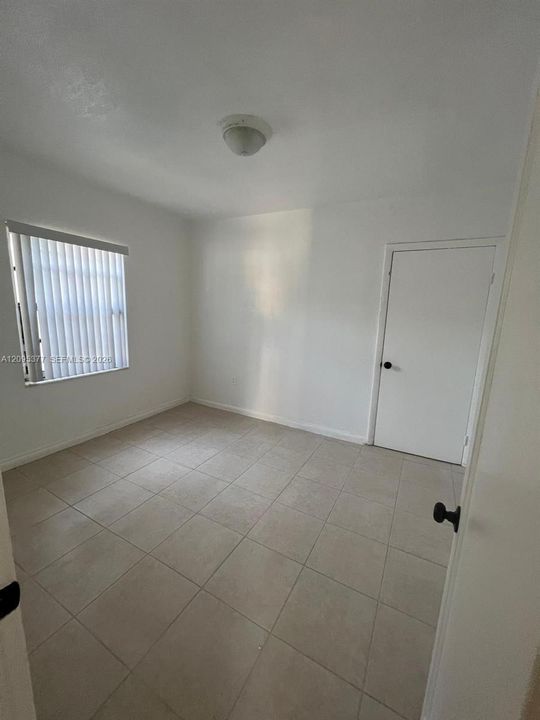 Neutral-toned tile flooring, white wall finish, interior door with black hardware, and a single window featuring vertical blinds