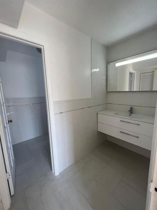 Wall-mounted vanity featuring a white composite countertop, integrated sink, and polished metal hardware, paired with a wall-spanning mirror with integrated lighting and full-height wall tiling