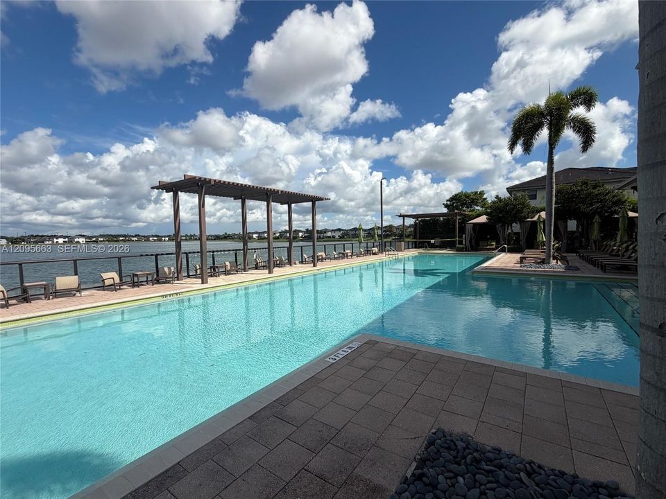 Waterfront swimming pool featuring paved decking, a wooden pergola, and metal perimeter railing