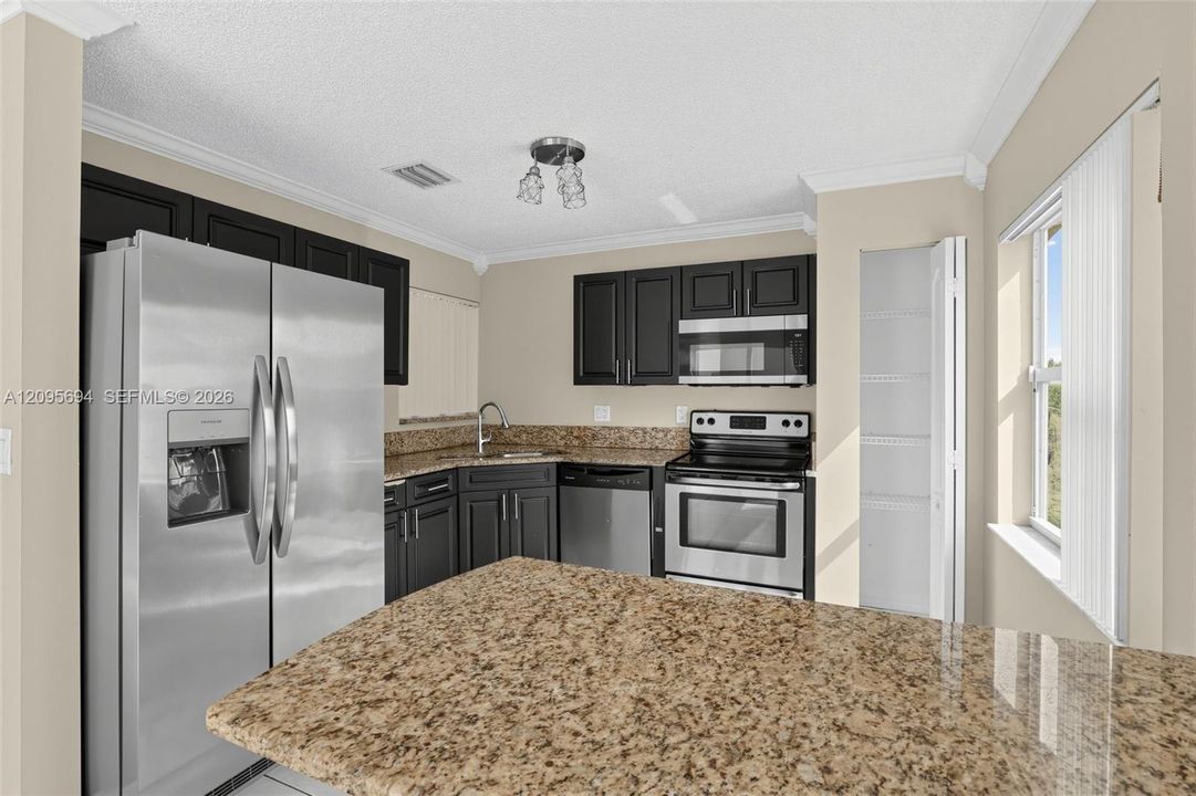 Kitchen featuring dark cabinetry, stone-finish countertops, stainless steel appliances, a built-in pantry, and crown molding