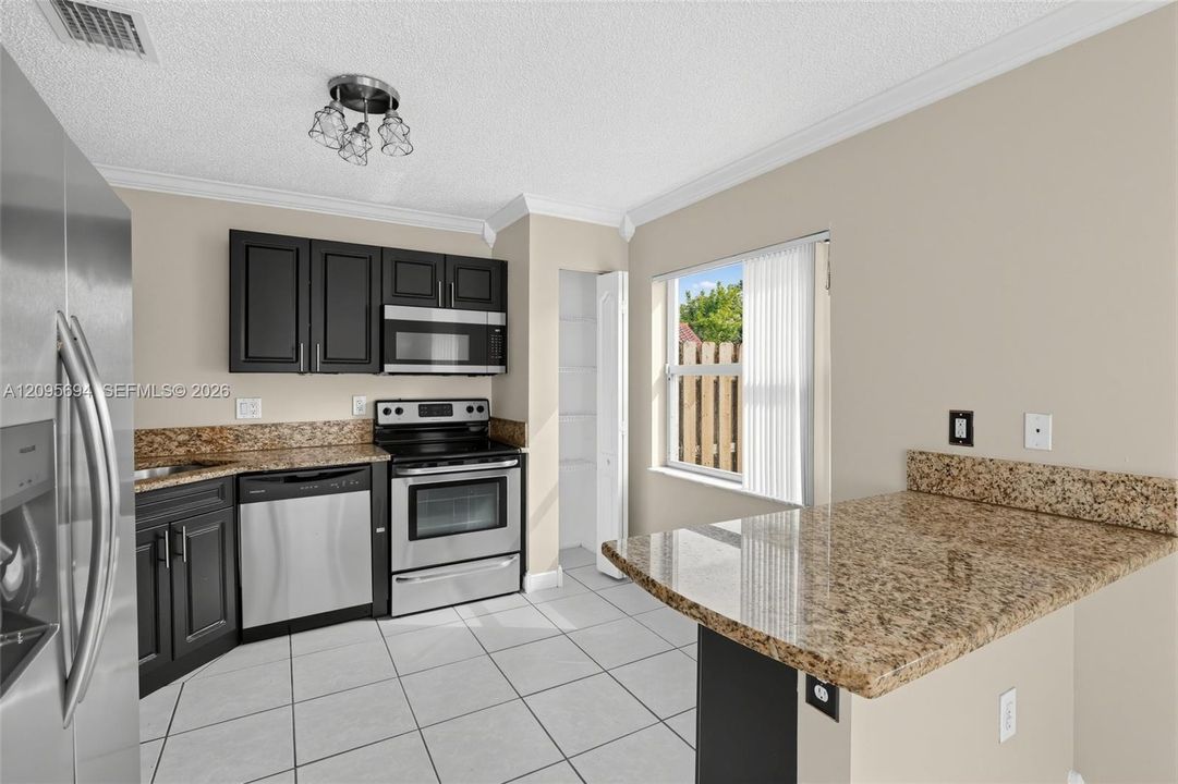 Kitchen featuring dark cabinetry, stone-surface countertops, stainless steel appliances, a built-in pantry, and tile flooring