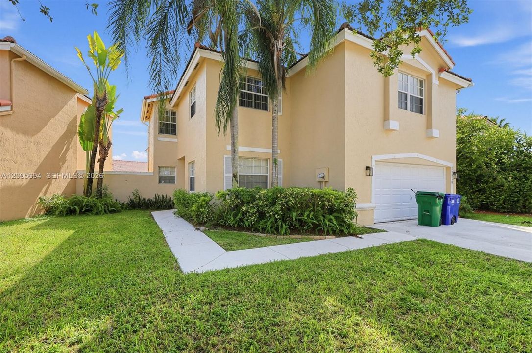 Two-story stucco exterior featuring a concrete tile roof, attached two-car garage, multi-pane windows, and concrete walkways set within a landscaped yard