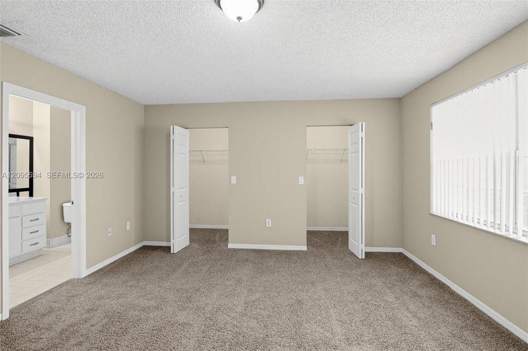 Room featuring neutral wall tones, plush wall-to-wall carpeting, dual closets with bi-fold doors, and a window with vertical blinds