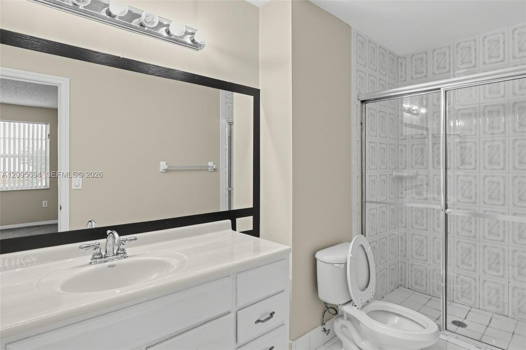 Bathroom featuring a white vanity with an integrated sink, a large framed vanity mirror, a multi-light fixture, and a tiled shower enclosure with sliding glass doors