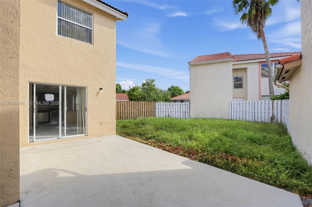 Rear exterior featuring a concrete patio, stucco siding, sliding glass doors, and a private fenced yard