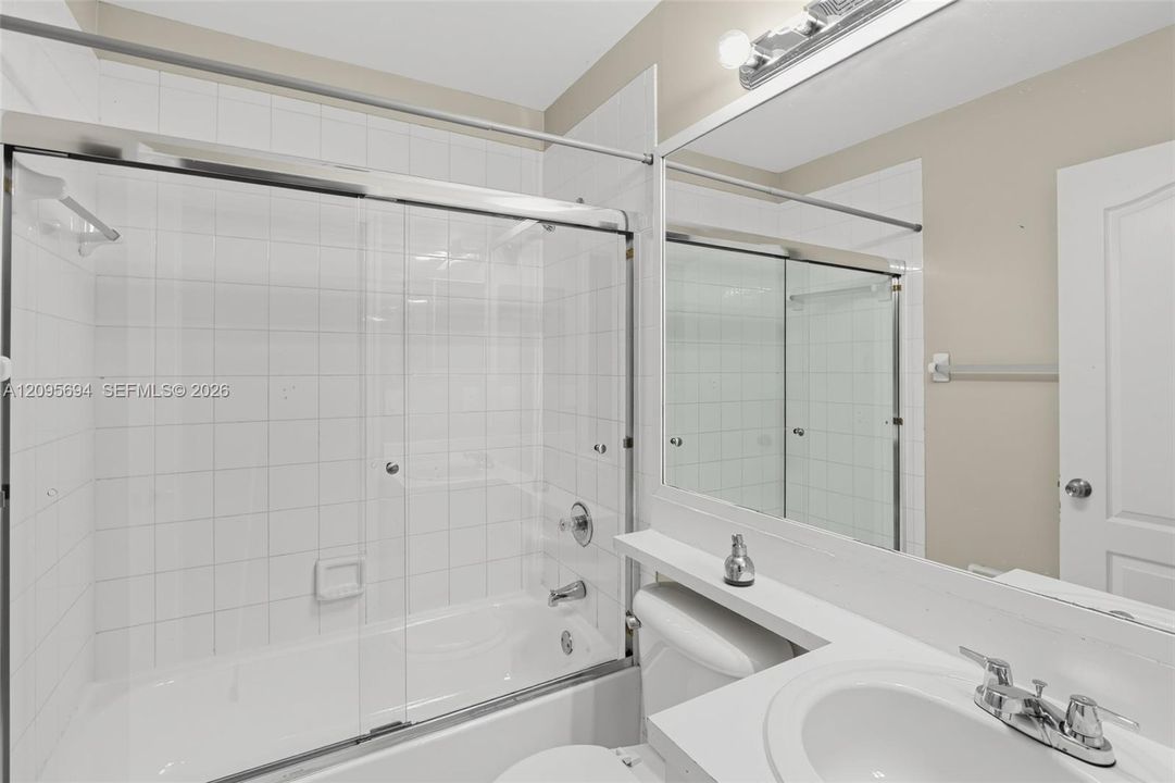 Bathroom featuring a tub-shower combination with glass sliding doors, white tile surround, a large vanity mirror, and an undermount sink with dual-handle faucet