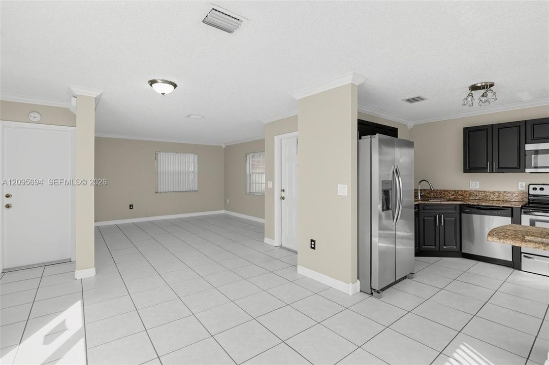 Kitchen area featuring dark cabinetry, stone-finish countertops, stainless steel appliances, and large-format tile flooring throughout